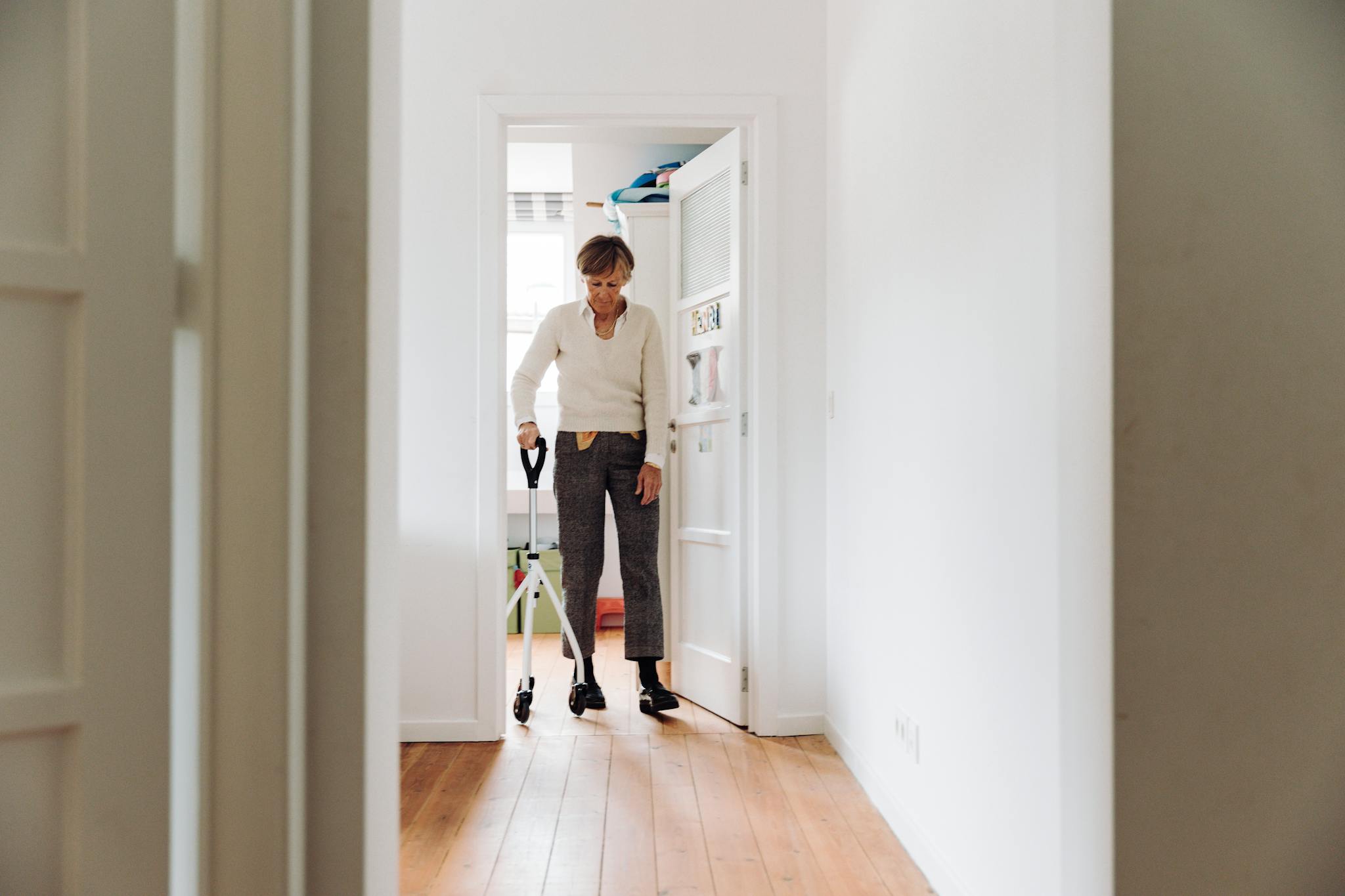 Senior woman walking with rollator in a brightly lit hallway for indoor mobility support.